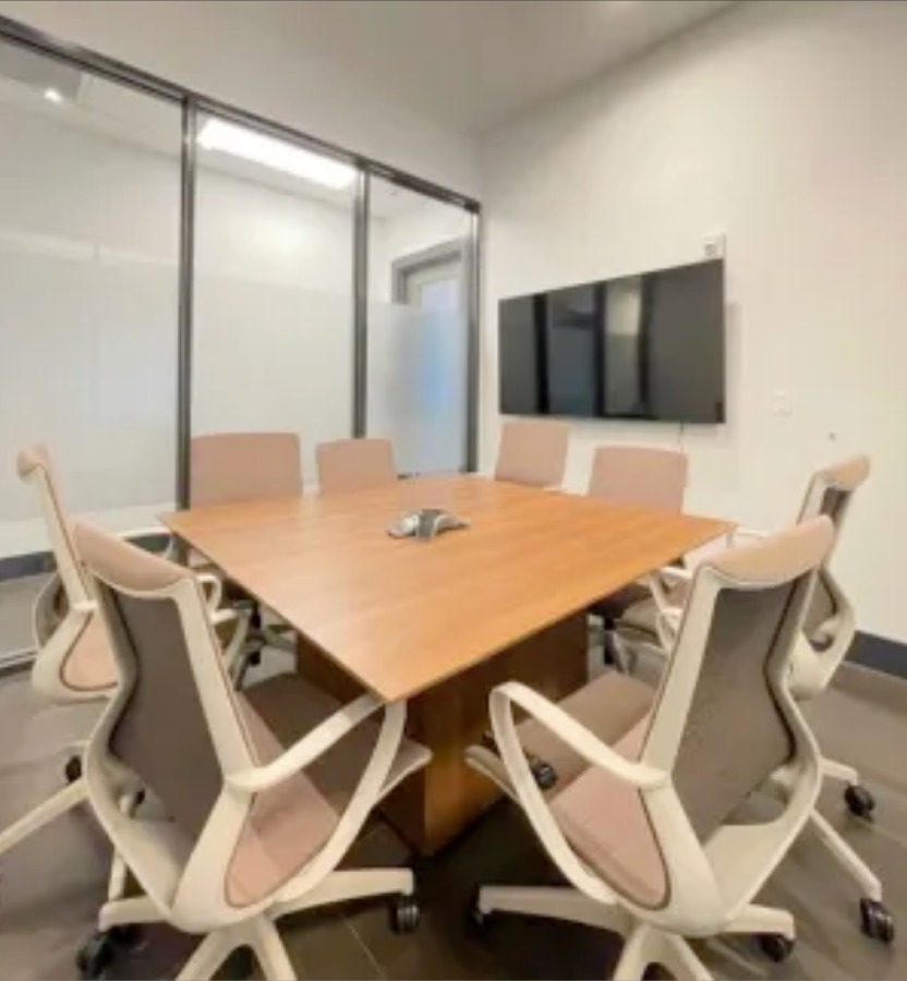 A modern meeting room with neutral colors, office chairs, equipment, and a glass facade.